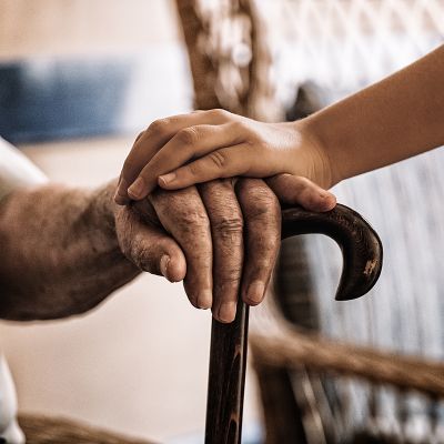 child's hand over old man's hand holding a cane.