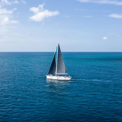 A snow-white yacht with bright sail t is sailing along the sea by, the backdrop of an azure sky.
